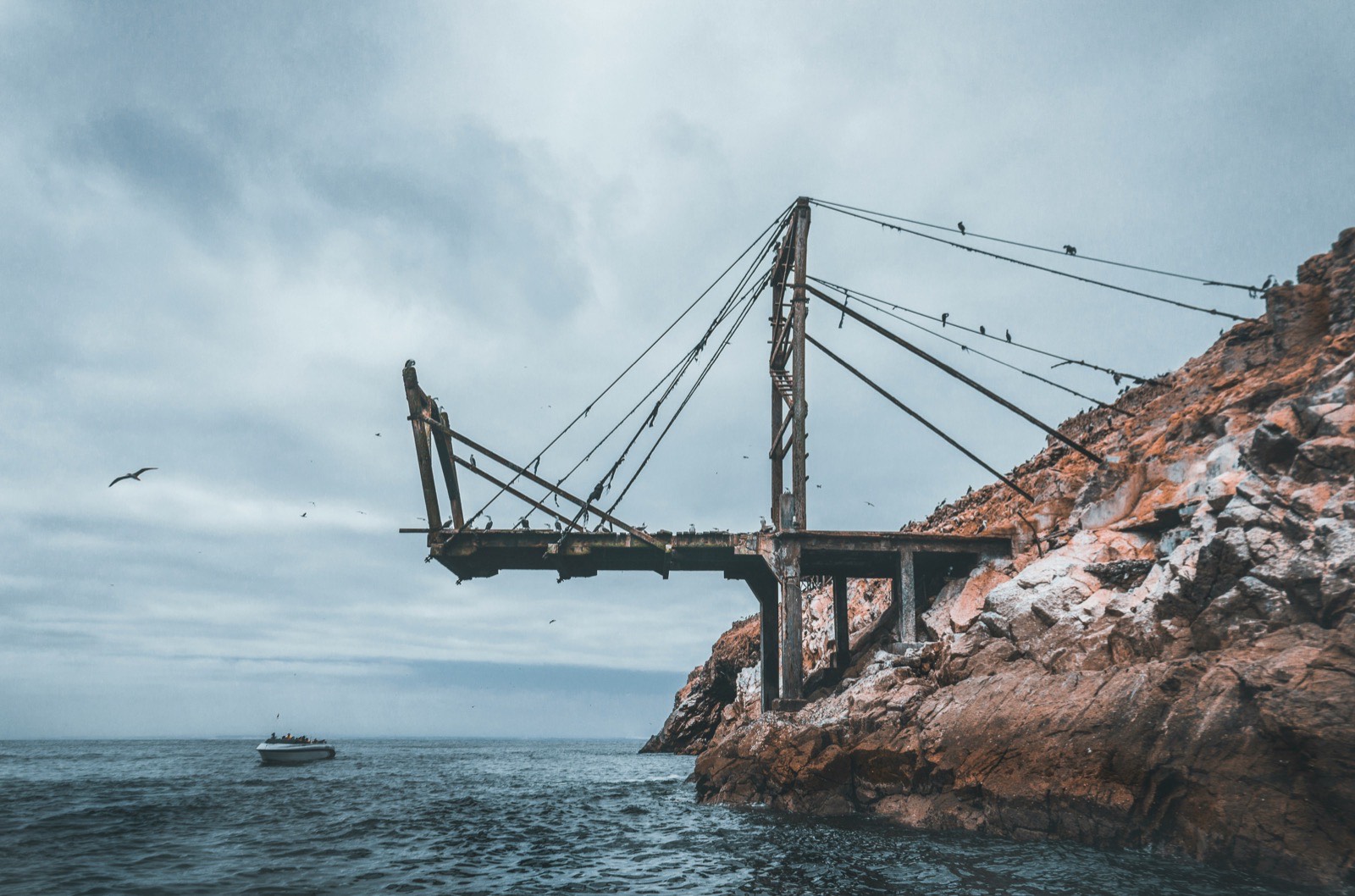 A weathered loading pier reaching out over the water from a rock face, with a small boat approaching
